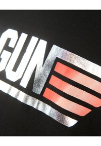 Mustan kankaan päällä on rohkeaa, metallinhohtoista hopeista tekstiä "GUN", jonka alla on punaisia ja oransseja raitoja. Pintakuvio on yleisesti sileä.