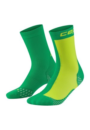 Coppia di calzini atletici a mezzocalf, uno verde uniforme e l'altro verde con un ampio pannello giallo e modelli testurizzati antiscivolo sulle suole.