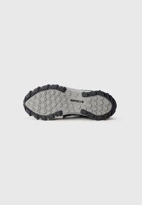 Suola di una scarpa da trekking Columbia grigia e nera con un motivo di battistrada robusto su sfondo bianco.