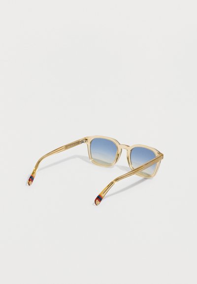 Námestíkové slnečné okuliare s priehľadným rámom v svetlo zlatej farbe a modrými šošovkami s prechodovým efektom. Bočnice majú viacfarebný pruhový detail.