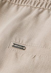 Béžová látka s texturovaným povrchem, se stříbrným štítkem s nápisem „Street One“, našitým na okraji kapsy. Hladký, nařasený pas.