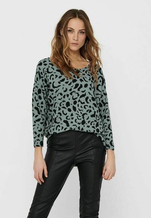 Grønn og svart leopardmønstret genser med vid halslinning og lange ermer, kombinert med svarte imitation skinnbukser. Myk strikket tekstur.