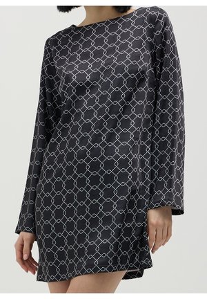 Frau trägt ein schwarzes, langärmeliges Minikleid aus Satin mit einem weißen, gepunkteten geometrischen Kettenmuster.