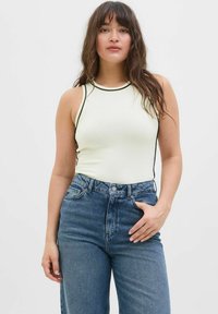 Hvid ærmeløs top med sort piping og en tætsiddende design, parret med høj-taljede blå denim jeans, der har forlommer.