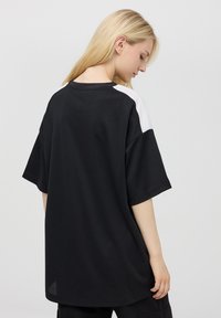 T-shirt nera oversize con maniche corte e scollo rotondo. Dettagli bianchi sulle spalle. Tessuto liscio, vestibilità rilassata.