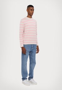 Svetlo roza in bela prugasta majica, kroj s krožno zasnovo, v kombinaciji s svetlo modrimi kavbojkami in belimi supergami. Tkanina se zdi mehka in sproščena.