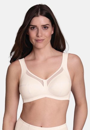 Vrouw met lang bruin haar die een lichtbeige beha met brede bandjes en een doorschijnend mesh detail aan de bovenkant van de cups draagt.