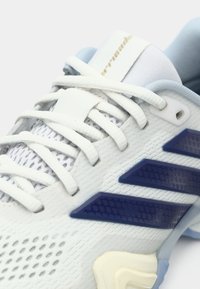 Baskets blanches avec des accents bleu clair, tige en maille texturée et bandes latérales bleu foncé. Comprend une languette et un système de laçage rembourrés.