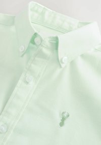 Világoszöld gombos ing, pamutból készült, hegyes gallérral, fehér gombokkal és egy kis hímzett homár logóval a mellrészen.