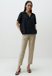 Camicia nera a maniche corte con scollatura a V e vestibilità rilassata, abbinata a pantaloni tapered beige chiaro. L'outfit presenta un design minimalista e senza fantasie.