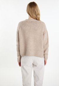 Beige gebreid trui met ribbelboord en manchetten, met een ontspannen pasvorm. Draag over lichtgekleurde broeken, waarbij een zachte, gestructureerde afwerking zichtbaar is.