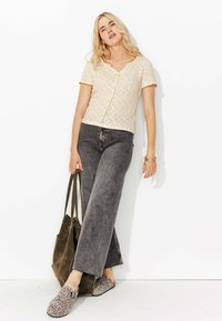 Haut en tricot crème à manches courtes avec col en V et fermeture à boutons, associé à un jean taille haute gris à jambes larges et des chaussures à enfiler à imprimé léopard.