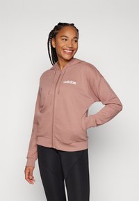 Rózsaszín zipzáras kapucnis pulóver, puha anyagból, húzózsinóros kapucnival és fehér "adidas" logóval a bal mellrészen. Hosszú ujjú, laza szabású.