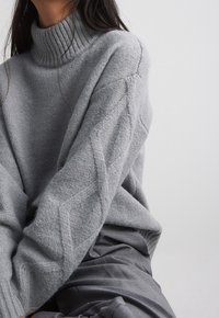 Pull gris clair en maille avec un col roulé côtelé et des motifs en losange sur les manches, fabriqué en tissu doux et texturé.