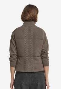 Brauner Strickpullover mit hohem Kragen, der ein strukturiertes Zopfmuster auf dem Rücken sowie gerippte Ärmelbündchen aufweist. Lässiger Schnitt.