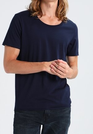 Laivastonsininen puuvillainen t-paita, jossa on lyhyet hihat, pyöreä pääntie ja istuva malli, yhdistetty tummiin farkkuihin. Tasainen pinta, ei näkyviä kuvioita.