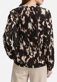 Haut à manches longues avec un motif abstrait noir, marron et crème, col rond et coupe décontractée. Le matériau semble doux et lisse.