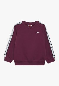 Sudadera marrón con el logo blanco de Kappa. Cuenta con mangas raglán y rayas laterales con patrón. Está hecha de un tejido suave y texturizado con un escote de patrón redondo.