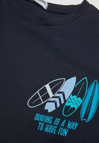 Navy blue bavlněné tričko s grafikou surfařských prken ve světle modré a bílé barvě, s textem "SURFING IS A WAY TO HAVE FUN" v tyrkysové.