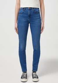 Jeans ajustados azules con cintura alta, confeccionados en denim. Presentan cinco bolsillos, un ligero desvanecido y una textura suave. Combinados con zapatillas negras.