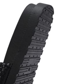 Zwarte sandaal met een gestructureerde band en een dikke, geribbelde rubberen zool met kleine afvoeropeningen. Het design is plat en open.