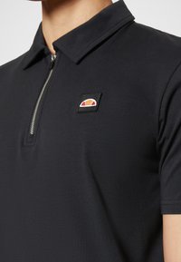 Čierna polokošeľa so zipsovým golierom, na ľavej strane hrude je výšivková nášivka s logom. Hladká tkanina s minimalistickým dizajnom.
