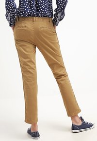 Chinos marron clair à coupe ajustée, avec des poches arrière, une texture lisse et des revers roulés, associés à des baskets en toile bleu marine.