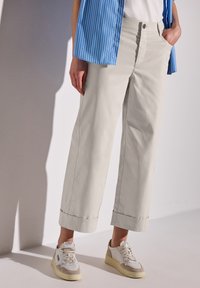 Ljust beige vida byxor med uppvikta fållar, med sidofickor och knappstängning fram. Parat med vita och beige sneakers.