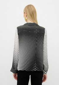 Camicetta a righe in bianco e nero con un design a pois sfumati, maniche lunghe, colletto e una texture lucida. Adatta per un abbigliamento casual.