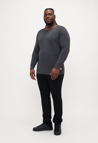 Grey long-sleeve sweater with a round neckline, paired with black jeans and black sneakers. The sweater features a textured knit finish.