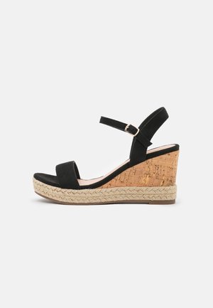 Sandale compensée en daim noir avec bride à la cheville, talon en liège et semelle plateforme en jute tressé, vue de profil sur fond blanc.