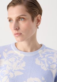 Lyseblå genser med blomstermønster i hvitt, rund hals og ribbede mansjetter. Laget av mykt, strukturert materiale.