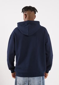 Ναυτικό μπλε φούτερ με μεγάλη, ρυθμιζόμενη κουκούλα. Διαθέτει άνετη εφαρμογή, μακριά μανίκια και ριμπ μανσέτες. Μαλακό, υφαντό ύφασμα.