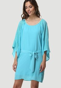 Vestido azul claro de corte holgado, de longitud corta, con mangas de encaje y un cinturón en la cintura. Presenta un escote redondo con detalles decorativos.