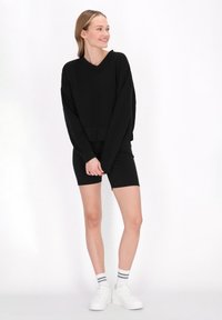 Hanorac negru supradimensionat cu mâneci lungi, design în formă de V, asortat cu pantaloni scurți negri. Purtați cu adidași albi și șosete până la glezne cu dungi.