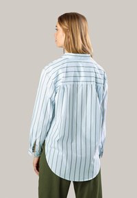 Light blue striped shirt with long sleeves, back pleat detail, rounded hem, and cuffed sleeves. Pairs with olive green pants.