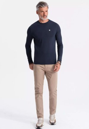 Marineblauwe longsleeve met ronde hals, gecombineerd met lichtbeige slim-fit broek. Casual sneakers maken de outfit af. Lichte stofstructuur.