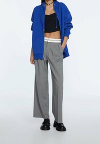 Felpa blu con zip, top corto nero, pantaloni grigi a gamba larga con pieghe e scarpe nere chunky, caratterizzati da un design semplice e linee pulite.
