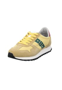 Sneaker giallo e beige con lacci gialli, suola nera, toppe con logo verde sui lati e dettaglio rosso sul colletto del tallone.