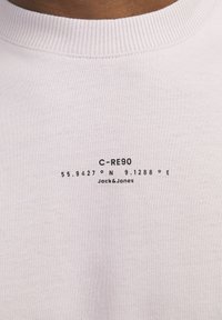 Vit bomullströja med rund ribbad halsringning. Tryckt svart text med koordinater och varumärket "Jack&Jones."