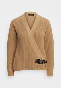 Beige stickad tröja med omslagdesign, prydd med en brun läderspänne vid midjan. V-ringning och vida ärmar.