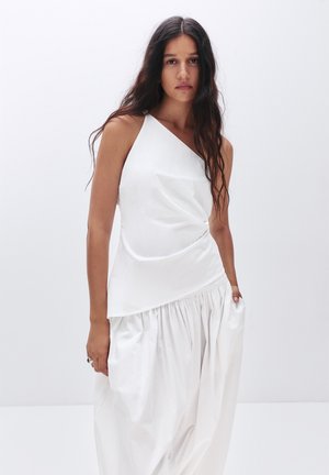 White sleeveless top featuring an asymmetrical design with draped texture, paired with a voluminous white skirt made from soft fabric.