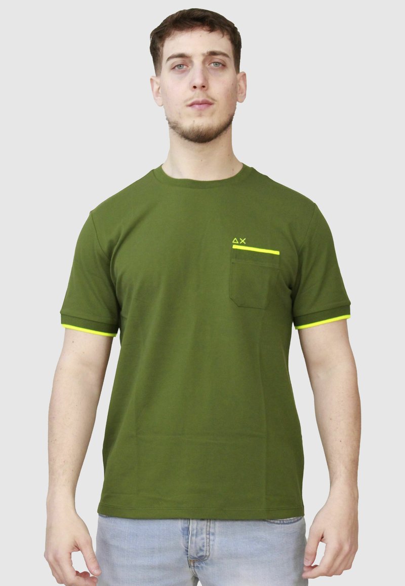 T-shirt verde oliva a maniche corte in tessuto morbido con accenti gialli sulle maniche e una tasca. Presenta un logo minimalista sul petto.