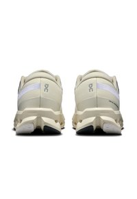 Baskets de sport beige clair avec une tige texturée, des accents de rayures blanches et des semelles rembourrées. Présente un logo et un motif de bande de roulement visible.