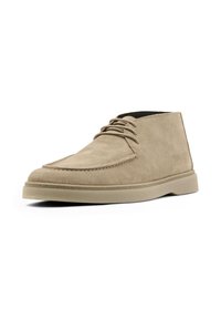 Bottines chukka en daim beige avec un bout rond, un design simple à lacets et une semelle en caoutchouc plate. Texture lisse avec des détails de couture minimes.
