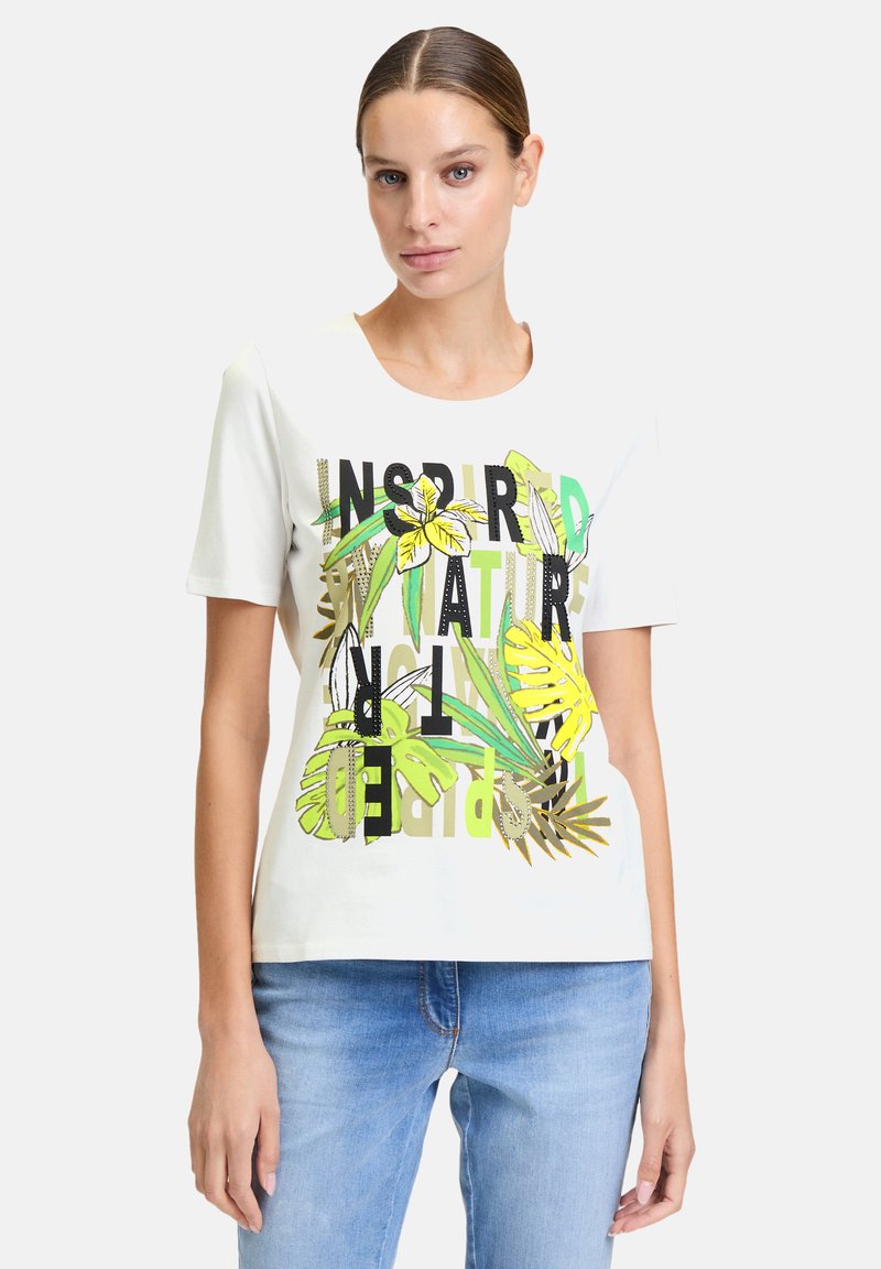 T-shirt en coton blanc avec des motifs botaniques verts et jaunes et un texte noir portant la mention "NATURE INSPIRE". Col rond classique et manches courtes.