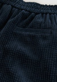 Marineblaue Cordhosen mit geripptem Textil, einem elastischen Bund und einer einzelnen Gesäßtasche, die mit einer sauberen Naht versehen ist.