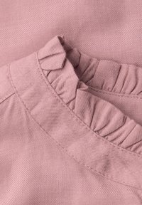 Tessuto rosa con una superficie texturizzata che presenta un bordo arricciato, creando interesse visivo e dimensione.