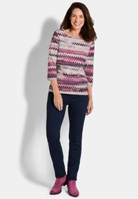 Bunt gemustertes Oberteil mit Zickzack-Muster aus leichtem Stoff, kombiniert mit dunklen Skinny Jeans und rosa Wildleder-Stiefeletten.