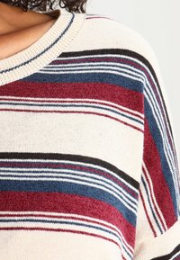 Knit sweater featuring horizontal stripes in beige, burgundy, blue, and black. Ribbed neckline. Soft, textured fabric.